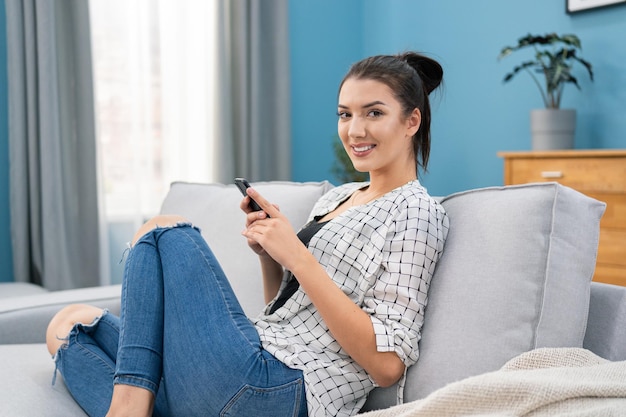 L'influenceuse est assise sur un canapé dans le salon, tenant le téléphone dans les mains, elle envoie des messages à son amie