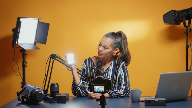 Influenceuse présentant une mini lumière led à usage professionnel dans son studio. Blogueur vidéo enregistrant un vlog avec l'utilisation d'équipements de produits technologiques en vidéographie et en photographie