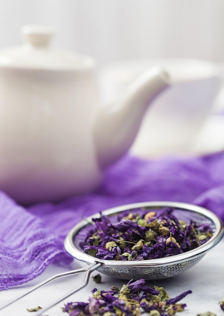 Infuseur à passoire avec thé en vrac de fleurs de mauve bleue sur tissu violet avec théière et tasse en céramique