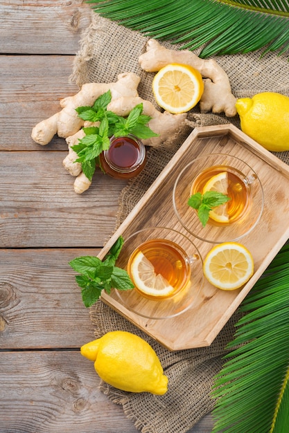 Infusion de boisson chaude en verre pour les journées d'automne hivernales contre la grippe froide. Tasse de thé au gingembre à la menthe, au citron et au miel sur une table en bois, mise à plat