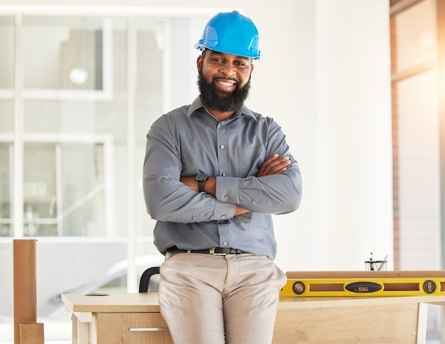 Photo ingénierie bras croisés et portrait d'un ouvrier du bâtiment confiant dans son bureau sourire heureux et professionnel industriel africain debout près d'un bureau dans un bâtiment industriel sur place