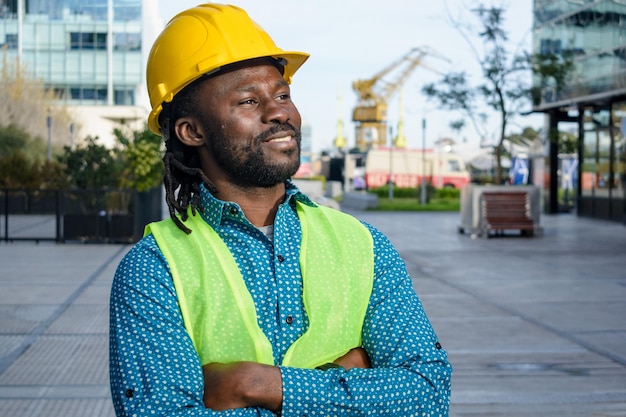 Un ingénieur africain, un ouvrier de la construction, se tient debout avec les bras croisés et sourit avec confiance.