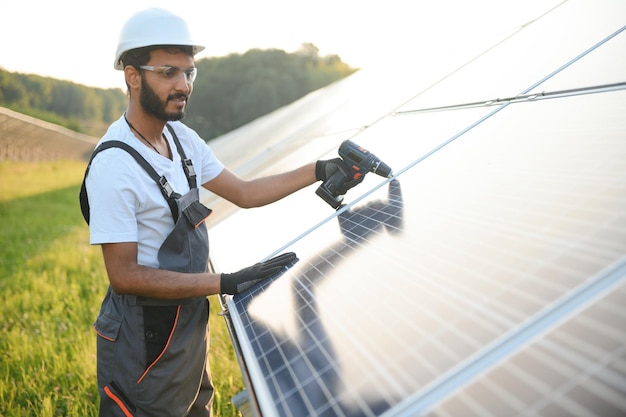 Ingénieur arabe en casque et combinaison brune vérifiant la résistance des panneaux solaires à l'extérieur homme indien travaillant sur la station