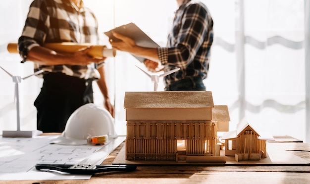 Ingénieur architecte de l'équipe professionnelle ou intérieur examinant le plan sur le bureau du lieu de travail derrière le modèle de maison au bureau