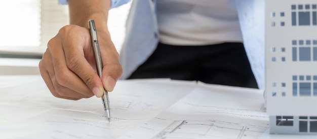 Photo ingénieur architecte professionnel ou main intérieure examinant le plan avec le modèle de construction sur le bureau du lieu de travail dans le centre de bureau au concept d'ingénierie de construction de l'entrepreneur de chantier