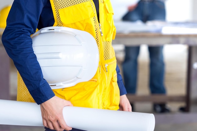 Ingénieur architecte tenant un casque de sécurité et un plan de dessin sur le chantier de construction