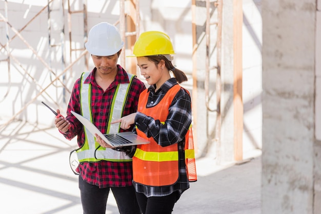 Un ingénieur asiatique contremaître ouvrier homme et femme travaillant sur un chantier de construction utilise un ordinateur portable et parle avec la radio, l'ingénierie tient l'ordinateur et la radio discute et contrôle l'employé ouvrier au bâtiment