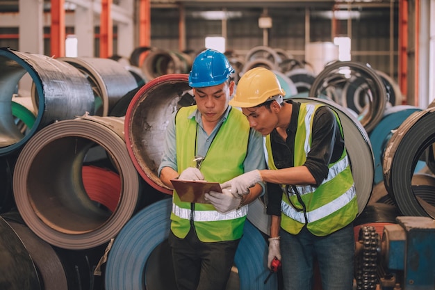 Ingénieur asiatique directeur d'usine et employé mécanicien dans un casque de sécurité parlant et inspectant à l'intérieur de l'usine