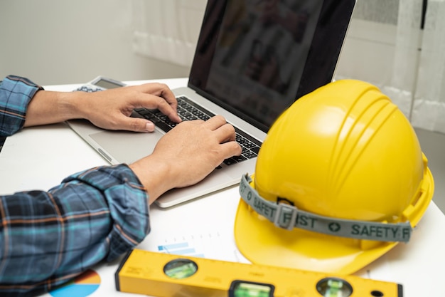 Ingénieur asiatique avec graphique de plan de projet de plan de maison architecturale et casque jaune et outils de construction d'ingénierie