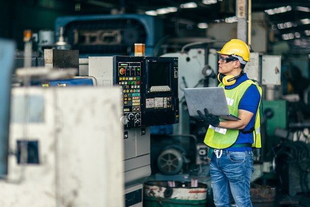 Ingénieur asiatique programmant la machine en usine avec un ordinateur portable pour configurer le processus du programme.