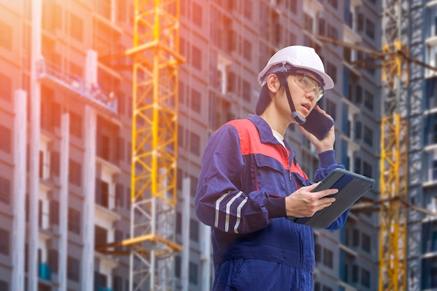 Ingénieur asiatique tenant une tablette informatique et parlant sur un smartphone tout en travaillant sur un chantier de construction