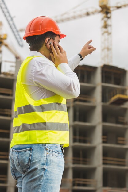 Ingénieur en casque rouge parlant par téléphone et pointant sur le chantier