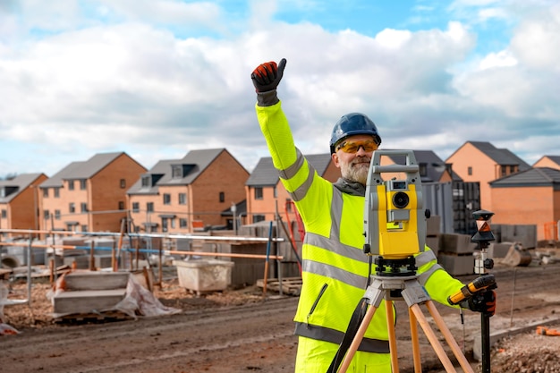 Photo ingénieur de chantier à hiviz travaillant sur un chantier de construction de maisons à l'aide d'un équipement d'arpentage moderne