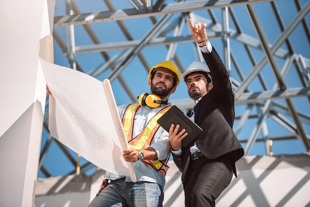 Ingénieur civil et responsable des travailleurs de la construction tenant une tablette numérique et des plans Ils envisagent le concept de travail d'équipe de coopération de la prochaine phase de construction