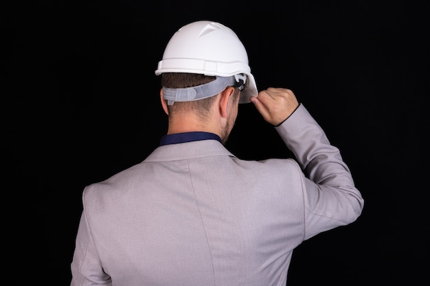 Un ingénieur constructeur se tient avec son dos avec un casque blanc sur fond noir