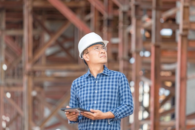 Ingénieur en construction homme vérifiant le projet sur le chantier Contremaître en casque sur le chantier de construction d'infrastructures Architecte avec une tablette numérique sur un chantier de construction