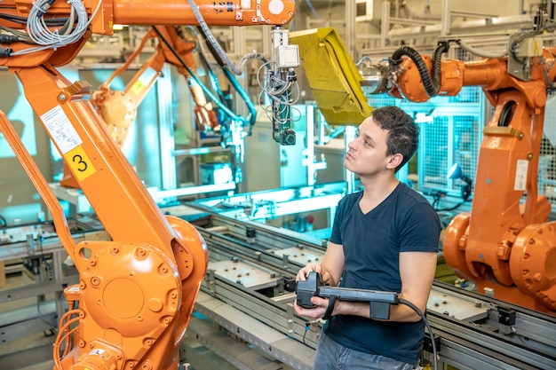 Ingénieur contrôle à l'aide de la télécommande d'un robot industriel en usine. Soudage et collage automatiques par automatisation et bras robotisés