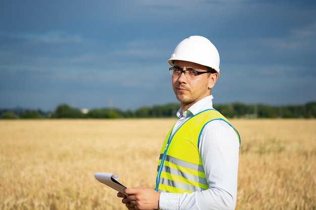 Un ingénieur dans un casque blanc et un gilet jaune se tient avec un dossier sur le terrain un agriculteur dans le f