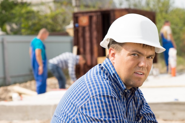 Ingénieur du bâtiment masculin d'âge moyen avec un casque blanc sur le site. En regardant la caméra.