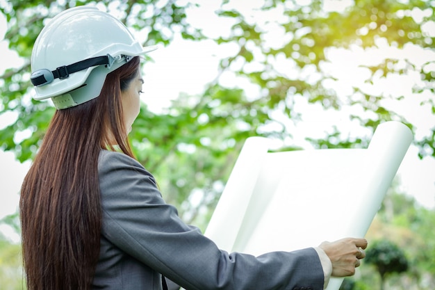 Ingénieur en environnement féminin vêtu d'un costume, coiffé d'un chapeau blanc, debout tenant un plan en papier