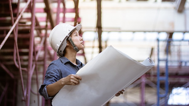 Ingénieur féminin portant un casque de sécurité tout en tenant le plan sur ses mains.