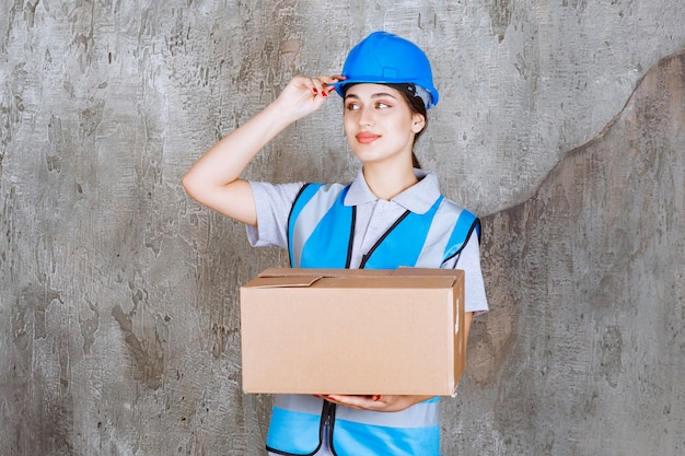 Ingénieur féminin en uniforme bleu et casque tenant un colis en carton