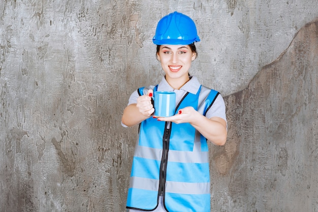 Ingénieur féminin en uniforme bleu et casque tenant une tasse de thé bleu.