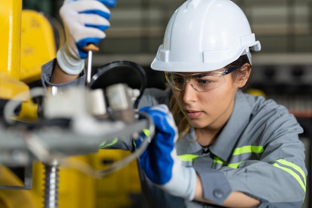 Ingénieur féminin vérifiant et maintenant la machine de bras de robot à l'usine