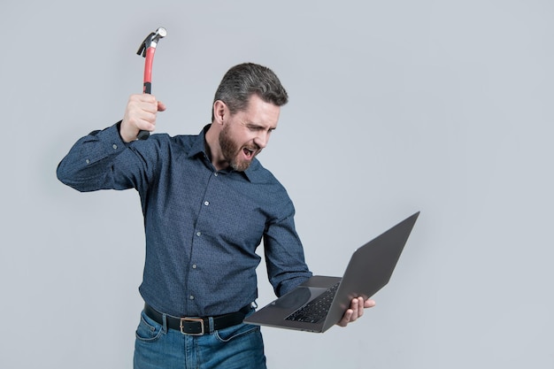 Ingénieur hurlant briser l'ordinateur portable avec la frustration de fond gris marteau