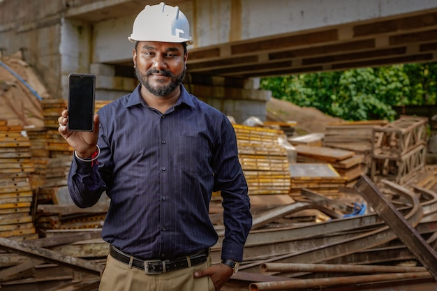 Ingénieur indien tenant mobile envoyer un message technologie internet Ingénieur construction projet de construction d'inspection