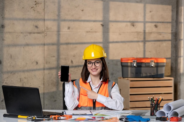 Ingénieur jolie jeune fille brune intelligente travailleuse civile en casque et gilet avec téléphone