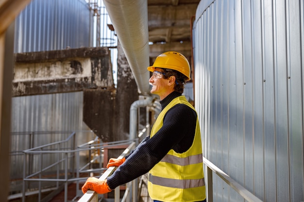 Ingénieur joyeux homme debout près d'un tuyau métallique à l'usine