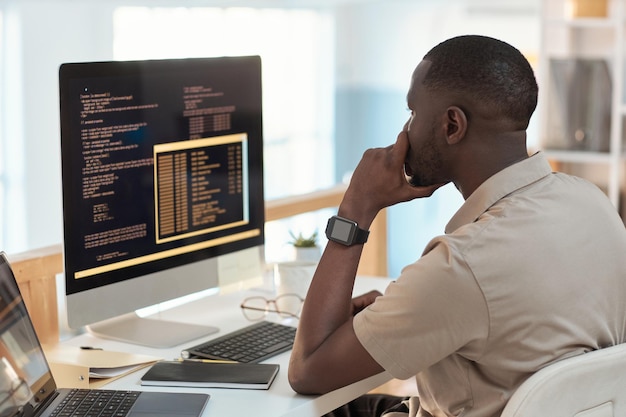 Ingénieur logiciel pensif vérifiant le code de programmation sur l'écran de l'ordinateur