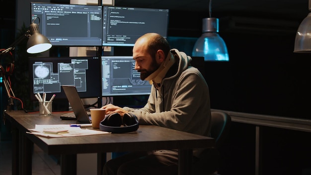 Ingénieur logiciel portant un collier cervical au bureau, tapant le code du serveur sur plusieurs écrans tard dans la nuit. Développeur d'applications avec une minerve médicale travaillant avec l'intelligence artificielle. Prise de vue à main levée.