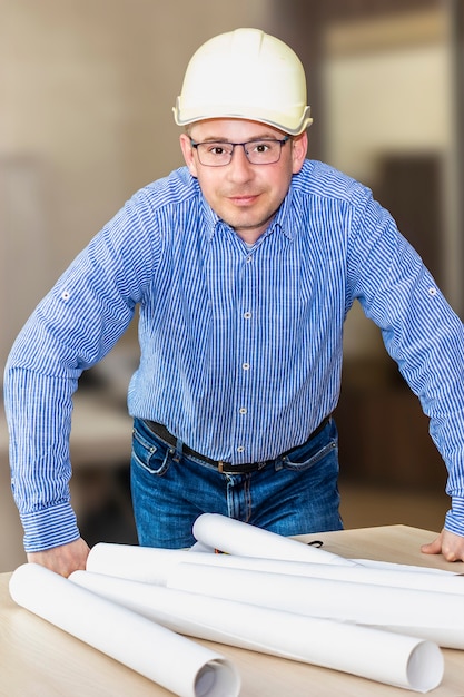 Photo un ingénieur avec des lunettes et un casque de chantier se pencha sur la table avec des documents. apporter des modifications aux dessins de construction. image verticale.