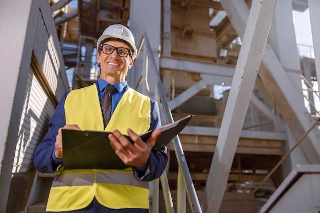 Ingénieur masculin gai avec des documents travaillant dehors à l'usine