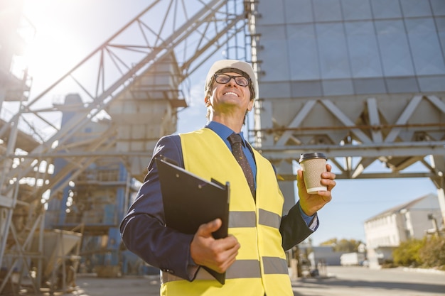 Ingénieur masculin gai tenant la tasse de café et les documents