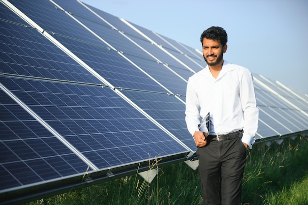 Ingénieur masculin vérifie une centrale solaire photovoltaïque et utilise une tablette d'enregistrement Indien en uniforme tenant une tablette