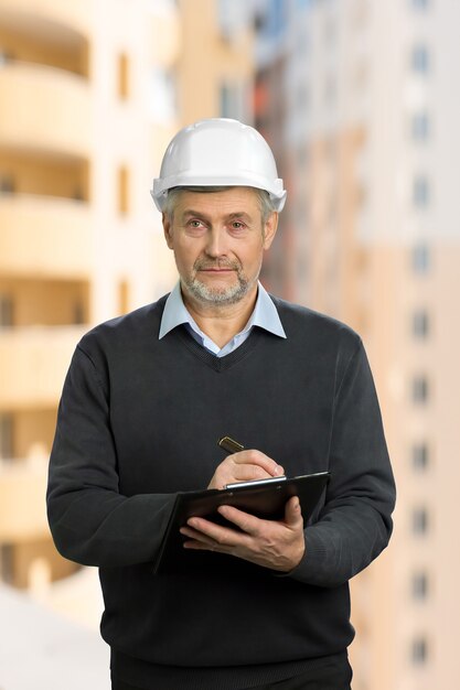 Ingénieur mature. Architecte principal écrivant sur le presse-papiers et regardant droit.