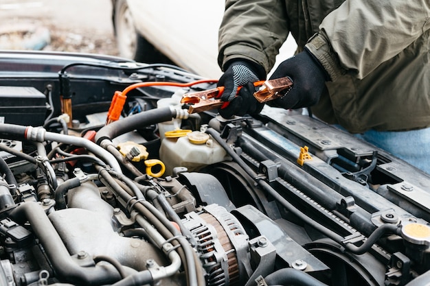 Ingénieur mécanicien chargeant la batterie de voiture avec de l'électricité à l'aide de câbles de démarrage à l'extérieur