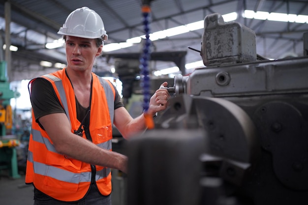 Ingénieur métallurgiste opérateur industriel expérimenté technicien ouvrier dans un casque de sécurité travaillant sur une machine de tour, homme professionnel dans l'atelier d'usine de fabrication de technologie industrielle