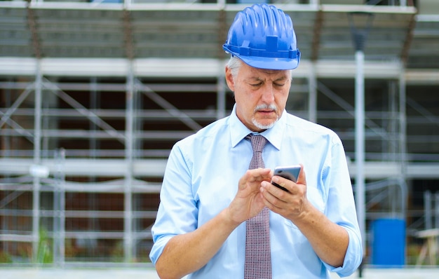 Ingénieur Senior Utilisant Son Smartphone En Plein Air Sur Un Chantier De Construction