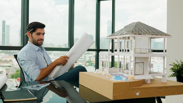 Ingénieur souriant à la recherche d'un plan de projet lors de la conception d'un modèle de maison