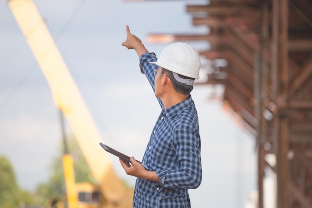 Ingénieur avec tablette sur le chantier de construction d'infrastructures Homme en chapeau dur vérifiant le projet sur le chantier