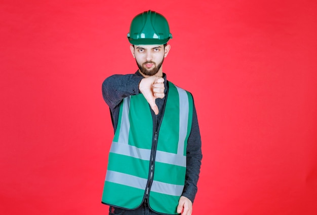 Photo ingénieur en uniforme vert et casque montrant le pouce vers le bas.
