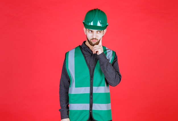 Photo ingénieur en uniforme vert et casque pensant et planifiant.