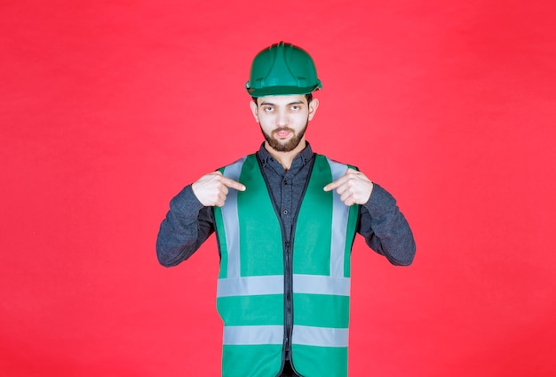 Ingénieur en uniforme vert et casque pointant sur elle-même.