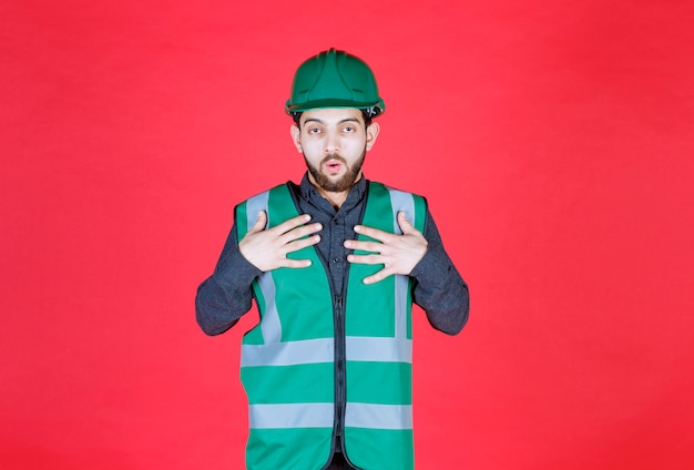 Ingénieur en uniforme vert et casque pointant sur elle-même.