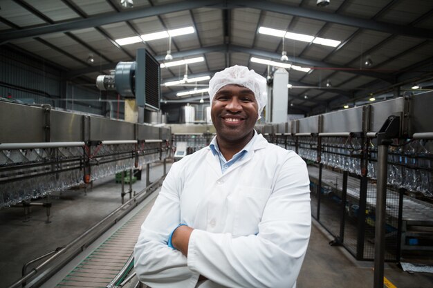 Ingénieur d'usine souriant debout avec les bras croisés dans l'usine de bouteilles