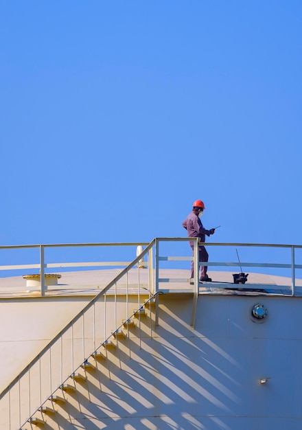 Ingénieur vérifiant la qualité de l'huile sur le dessus du réservoir de stockage de mazout contre un ciel bleu clair